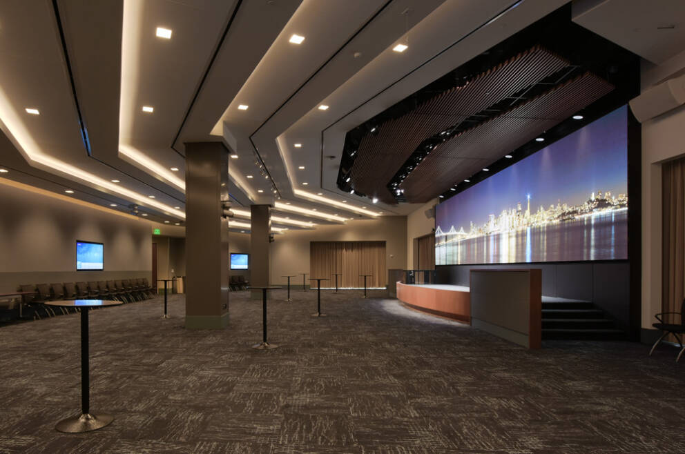 A large presentation space with circular tables in it. There is a small stage with a 40' LED display behind it. It has an image of the SF skyline.